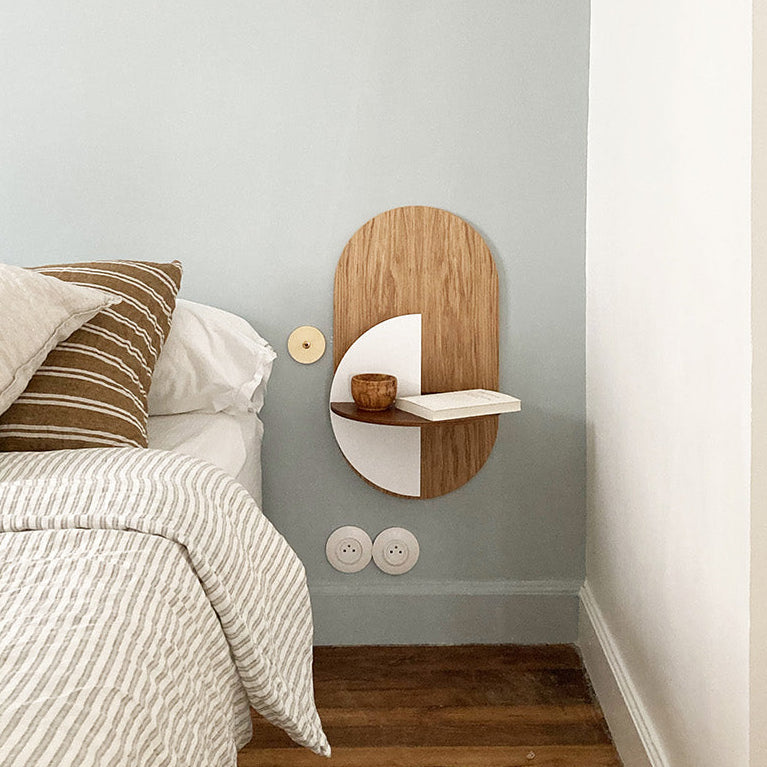 Wooden wall shelf mounted on a gray wall above a bed with striped bedding.