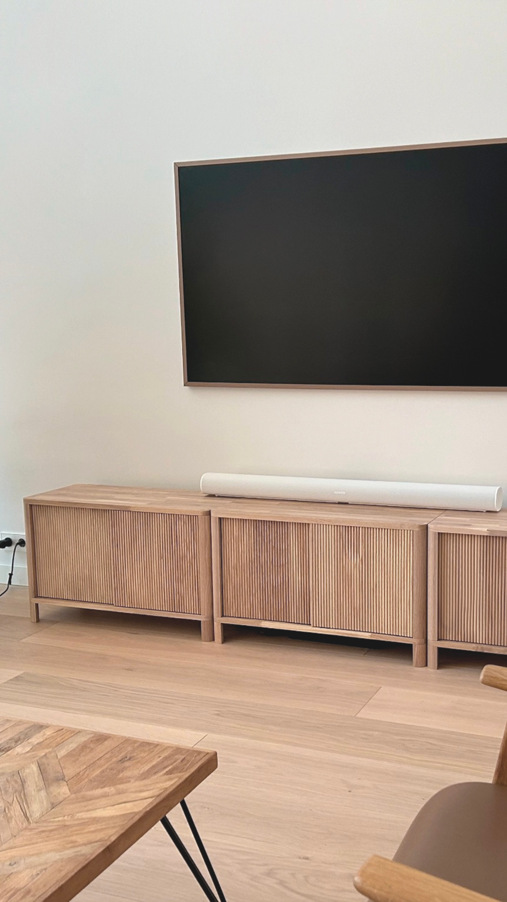 Wooden TV stand with a large flat-screen TV mounted on the wall in a minimalistic room.