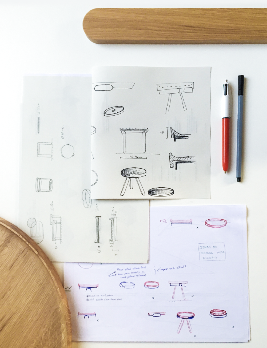 Design sketches of stools on a white surface with a pen and wooden object.